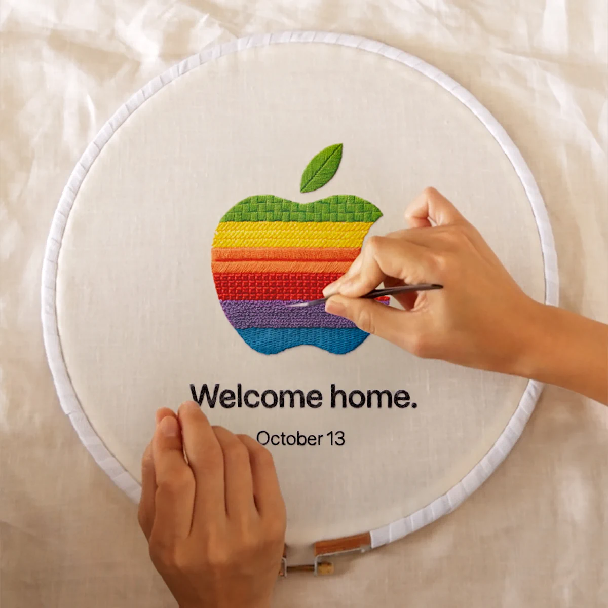 Apple公式の動画に登場する、虹色のリンゴを刺繍した「Welcome home. October 13」のティザー画像